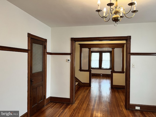 hall featuring dark wood-type flooring, baseboards, and an inviting chandelier