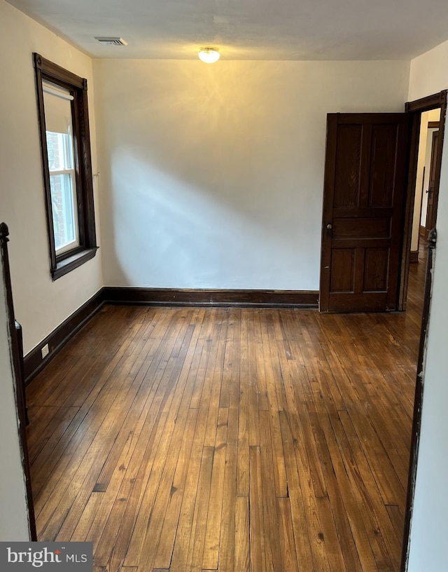 empty room featuring a barn door, wood-type flooring, visible vents, and baseboards