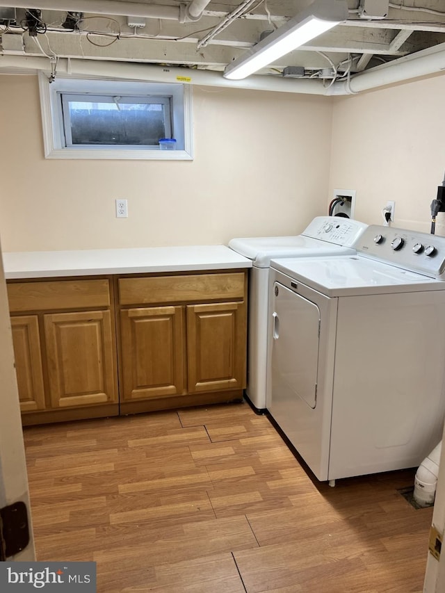 clothes washing area with cabinet space, light wood-style flooring, and separate washer and dryer