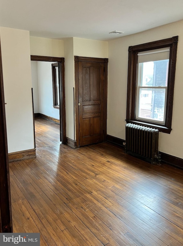 unfurnished bedroom with radiator heating unit, wood-type flooring, and baseboards