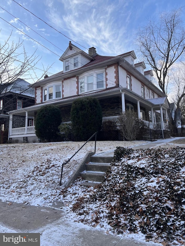 snow covered property with a porch, a chimney, and brick siding