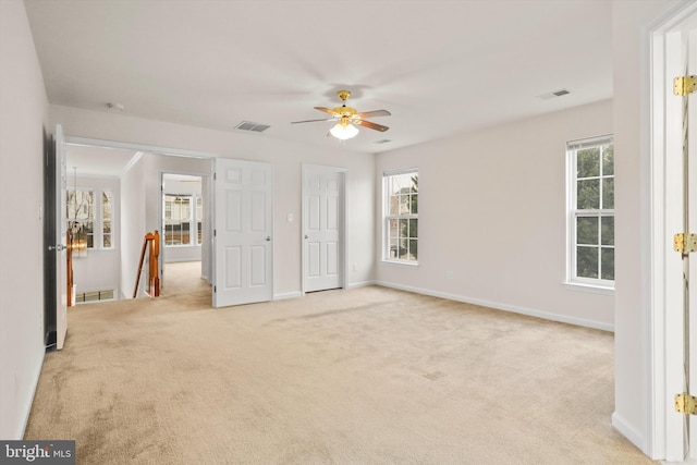 unfurnished bedroom featuring ceiling fan, multiple windows, and light carpet