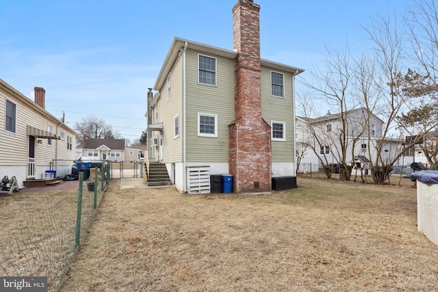 back of house featuring a yard, a chimney, central AC, fence, and a residential view