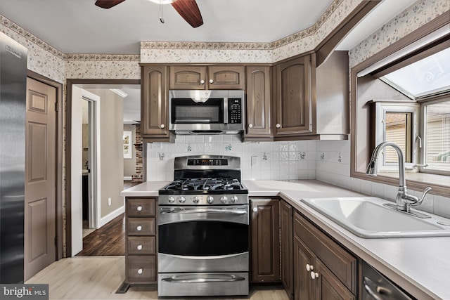 kitchen featuring light countertops, appliances with stainless steel finishes, a sink, dark brown cabinets, and wallpapered walls