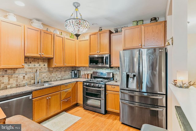 kitchen with stainless steel appliances, light stone countertops, sink, backsplash, and pendant lighting