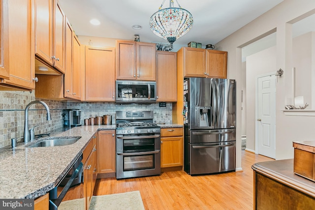 kitchen with appliances with stainless steel finishes, sink, decorative light fixtures, light hardwood / wood-style floors, and tasteful backsplash