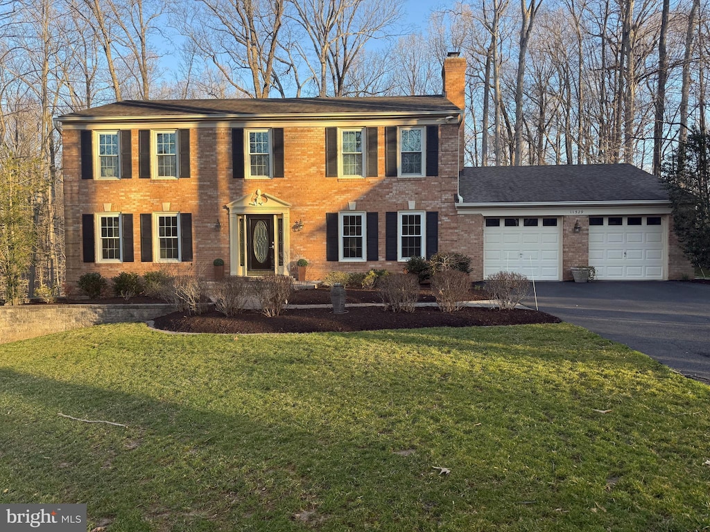 colonial inspired home with brick siding, driveway, a front yard, and a garage