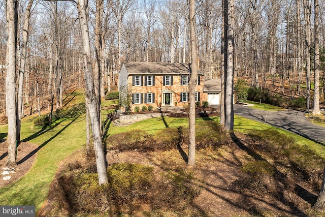 view of front of house featuring a front yard, an attached garage, a view of trees, and aphalt driveway