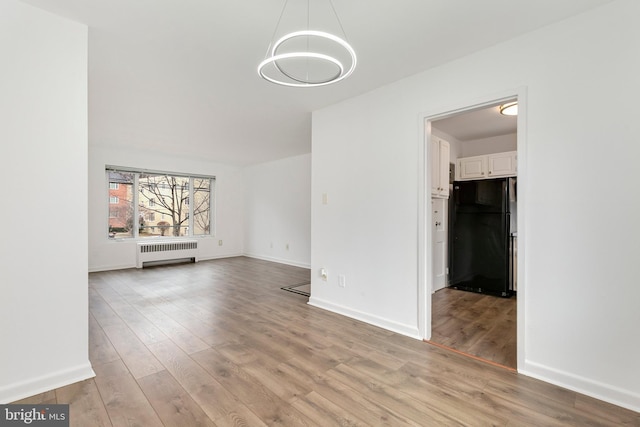 unfurnished living room with baseboards, radiator heating unit, and light wood-style floors