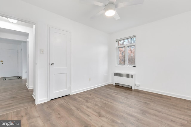 empty room with radiator, light wood finished floors, ceiling fan, and baseboards