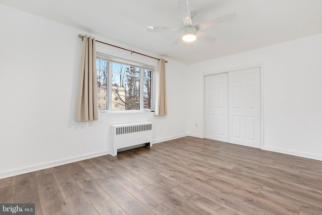 unfurnished bedroom with radiator heating unit, a closet, light wood-style flooring, and baseboards