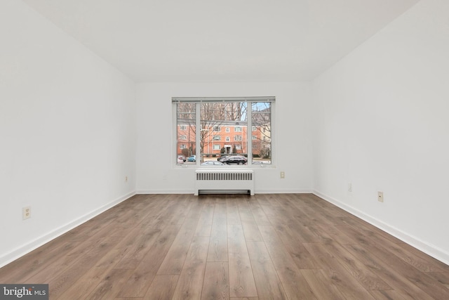 unfurnished room featuring radiator heating unit, baseboards, and wood finished floors