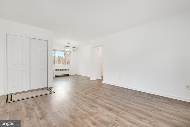 unfurnished living room featuring baseboards, an AC wall unit, light wood-style flooring, and radiator