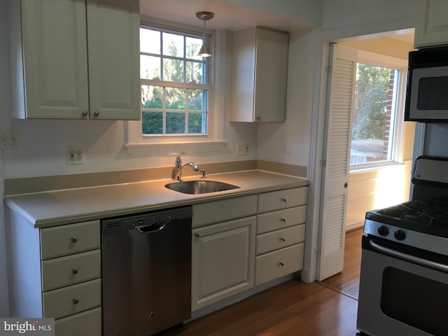 kitchen with a wealth of natural light, sink, white cabinetry, stainless steel appliances, and hanging light fixtures