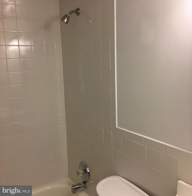 bathroom with toilet, tile walls, and tiled shower / bath combo