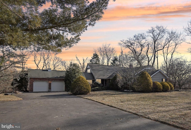 view of front of property featuring aphalt driveway, brick siding, a chimney, and an attached garage