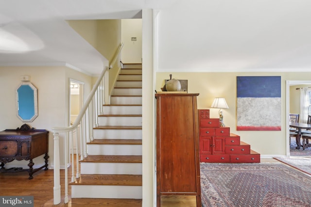 staircase with ornamental molding and wood finished floors