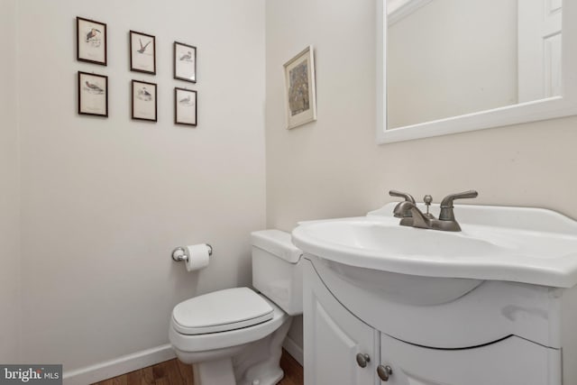 half bathroom featuring toilet, wood finished floors, vanity, and baseboards