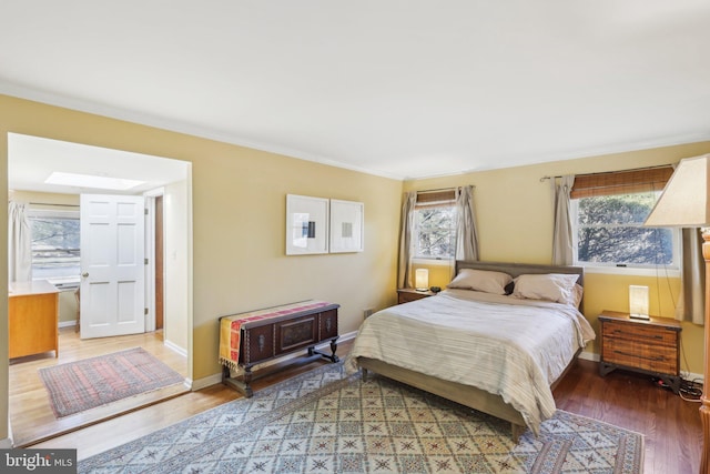 bedroom with light wood finished floors, a skylight, baseboards, and ornamental molding