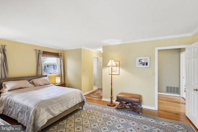 bedroom featuring ornamental molding, light wood-type flooring, visible vents, and baseboards