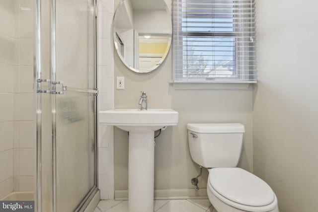 bathroom featuring toilet, a shower with door, baseboards, and tile patterned floors