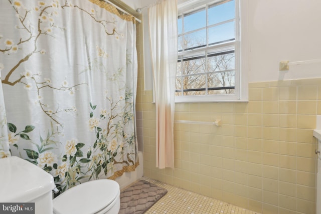 bathroom featuring wainscoting, shower / bath combo with shower curtain, toilet, and tile walls