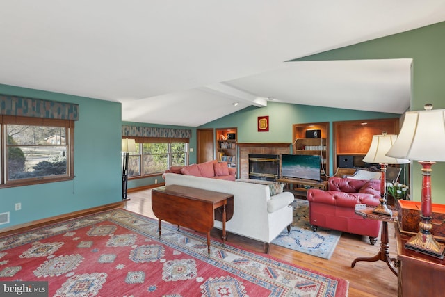 living area featuring visible vents, baseboards, a glass covered fireplace, wood finished floors, and vaulted ceiling