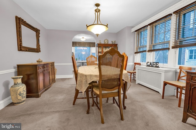 dining space with baseboards, arched walkways, and light colored carpet