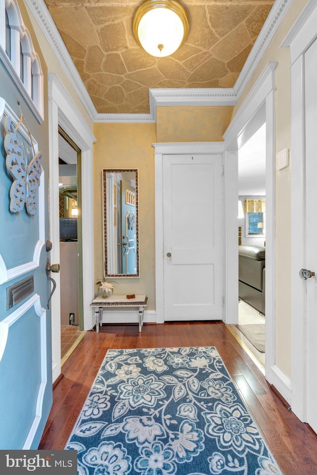 foyer with baseboards, wood finished floors, an ornate ceiling, and crown molding