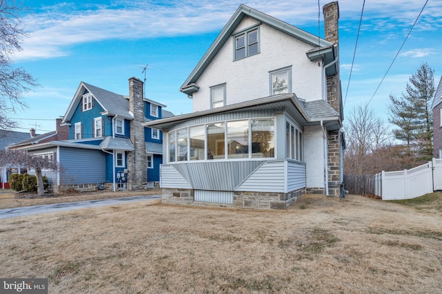 rear view of house featuring fence, a chimney, and a lawn