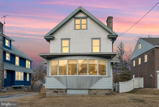 rear view of property featuring a chimney, fence, a lawn, and stucco siding