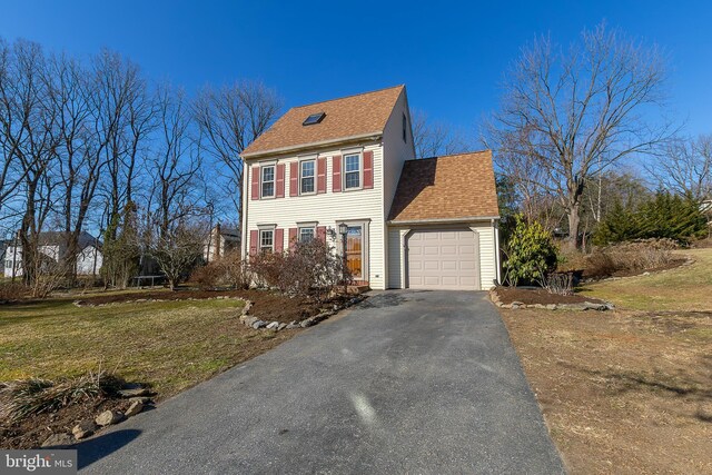 colonial house featuring an attached garage, a shingled roof, a front lawn, aphalt driveway, and a trampoline