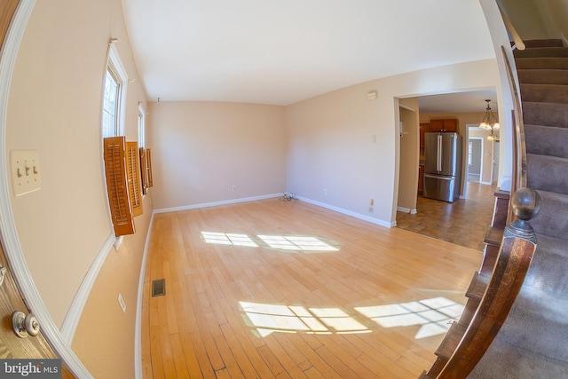 unfurnished living room featuring light wood-type flooring, stairway, and visible vents