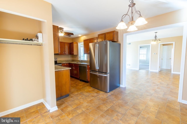 kitchen featuring brown cabinets, ceiling fan with notable chandelier, appliances with stainless steel finishes, baseboards, and hanging light fixtures