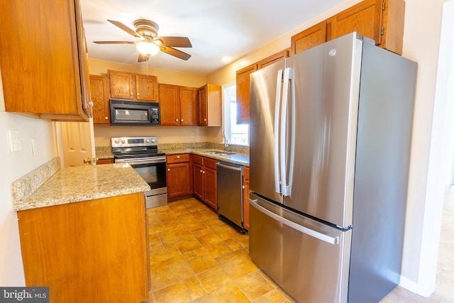 kitchen with a ceiling fan, a sink, light stone counters, appliances with stainless steel finishes, and brown cabinetry