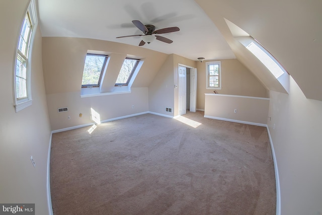 bonus room featuring a ceiling fan, baseboards, visible vents, carpet floors, and lofted ceiling with skylight