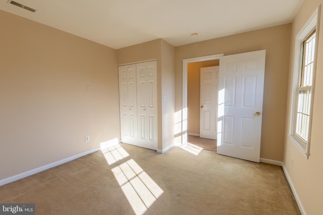 unfurnished bedroom with visible vents, light carpet, baseboards, and a closet