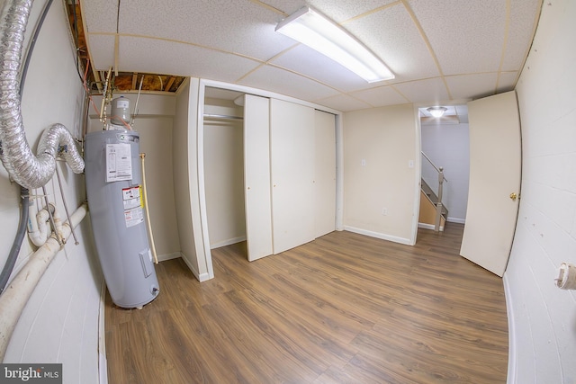 finished basement with water heater, a paneled ceiling, and wood finished floors