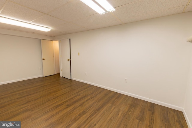 empty room featuring a drop ceiling, baseboards, and dark wood-style flooring