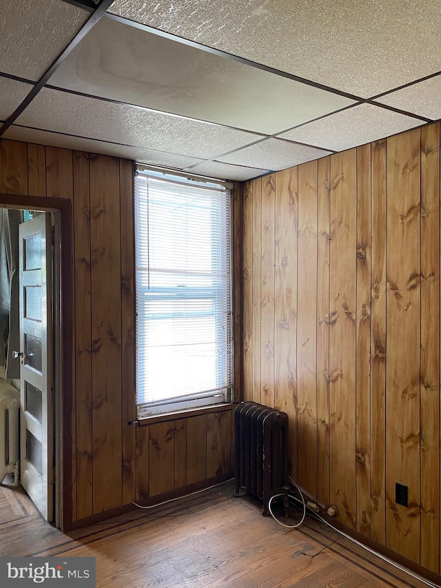 unfurnished room with a paneled ceiling, radiator, hardwood / wood-style floors, and wood walls