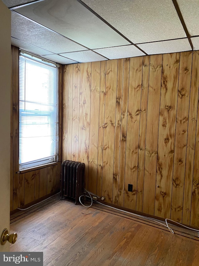 unfurnished room with a paneled ceiling, radiator, hardwood / wood-style floors, and wooden walls