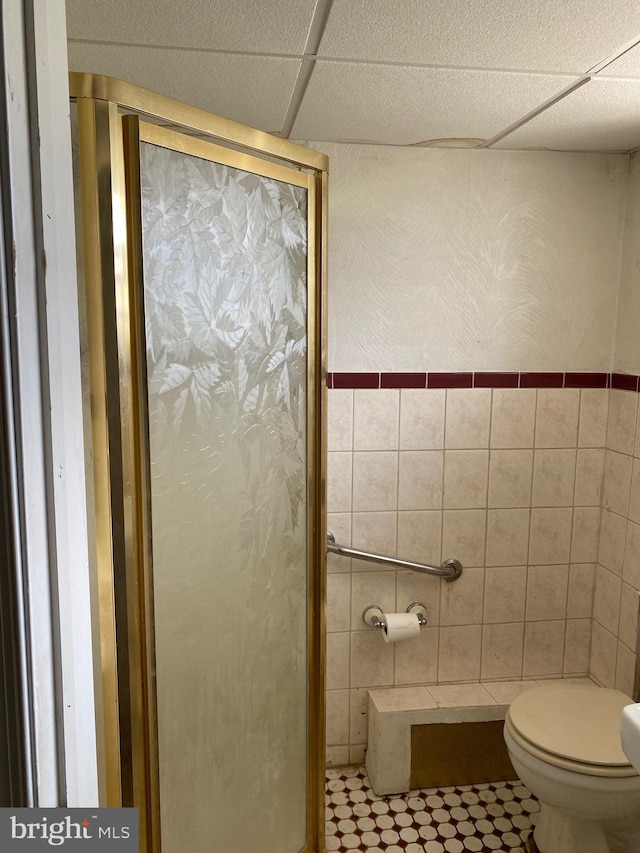 bathroom with a paneled ceiling, toilet, tile walls, and a shower with shower door