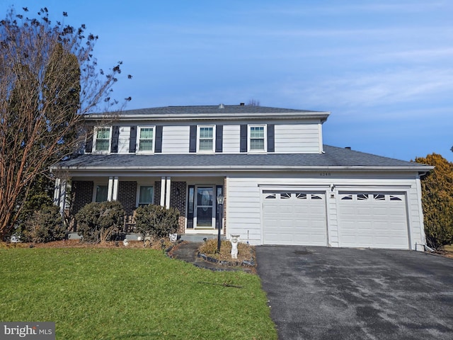 traditional home featuring an attached garage, driveway, brick siding, and a front yard