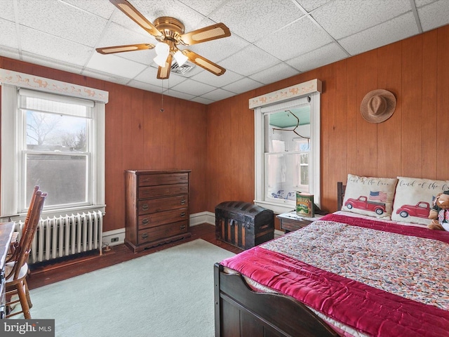 bedroom with wood walls, a drop ceiling, visible vents, and radiator