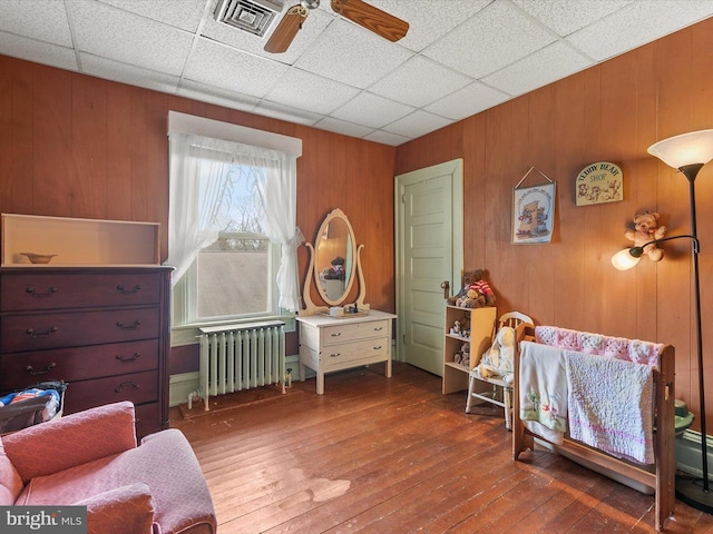 living area featuring a paneled ceiling, visible vents, radiator heating unit, a ceiling fan, and wood finished floors