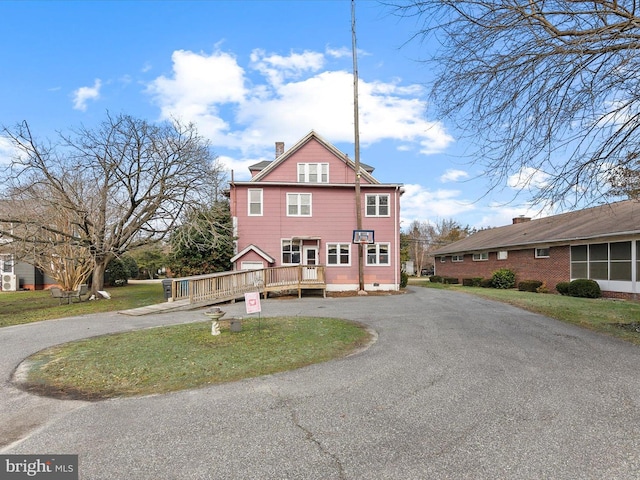 view of front of home featuring a front yard, a chimney, aphalt driveway, and a wooden deck