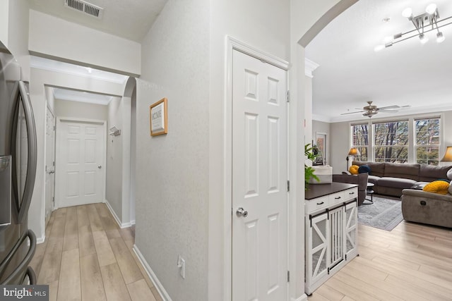 hallway featuring light wood-type flooring, visible vents, arched walkways, and ornamental molding