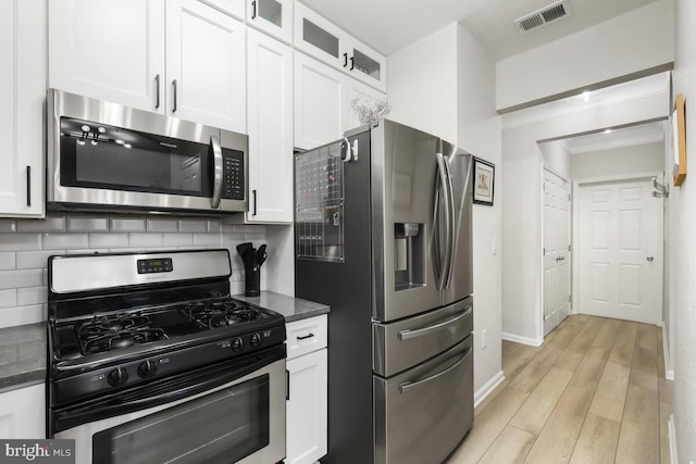 kitchen with stainless steel appliances, visible vents, glass insert cabinets, white cabinetry, and dark stone countertops