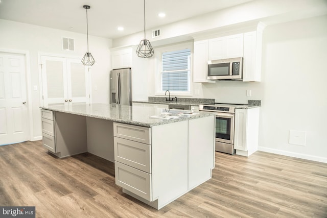 kitchen with visible vents, light wood-style flooring, appliances with stainless steel finishes, a center island, and a sink