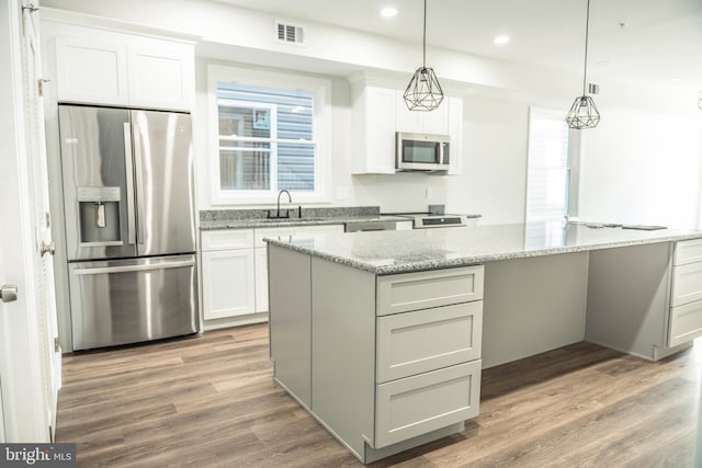 kitchen featuring stainless steel appliances, wood finished floors, a sink, visible vents, and pendant lighting